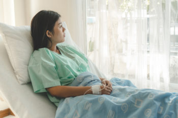 young woman sitting on the bed and looking outside window in hospital worry about her illness